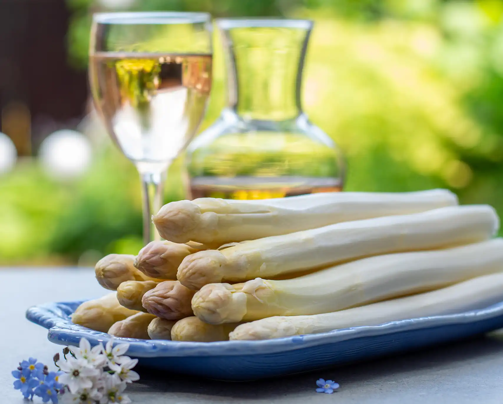Weißwein in Karaffe und Glas neben einem Teller mit weißem Spargel